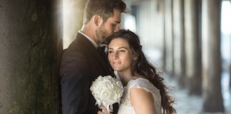 Two lovers embrace by the pier ocean with tuxedo and wedding dre