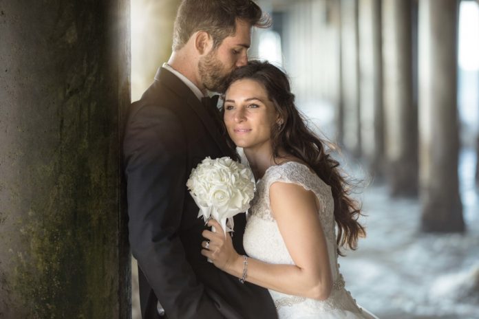 Two lovers embrace by the pier ocean with tuxedo and wedding dre